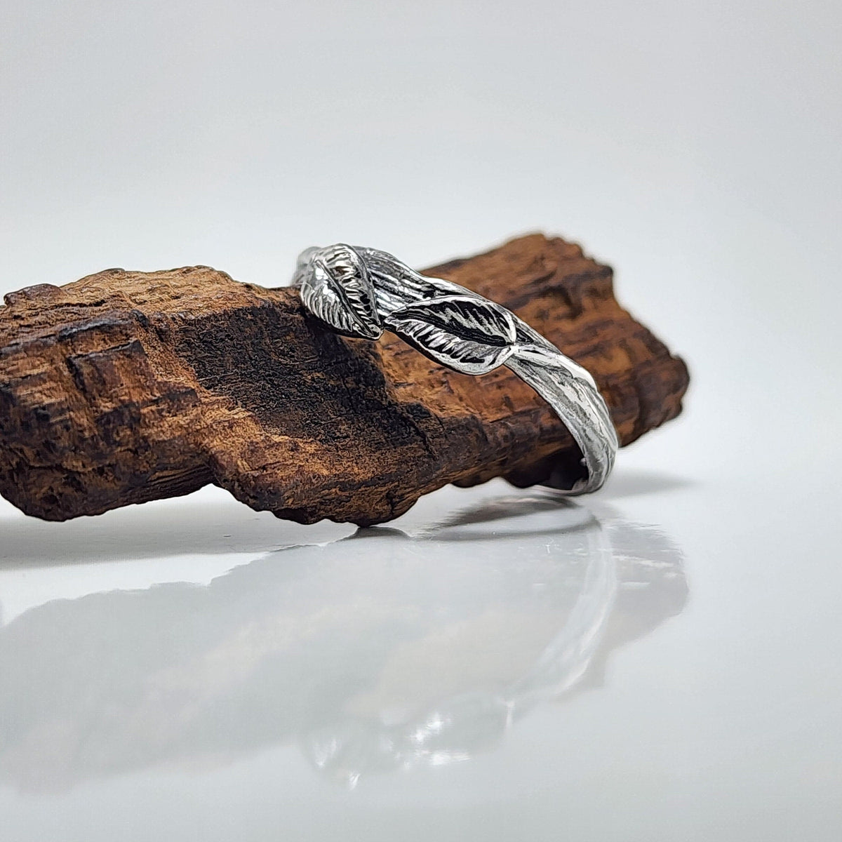 Silver ring with feather design on a wooden block against a white background