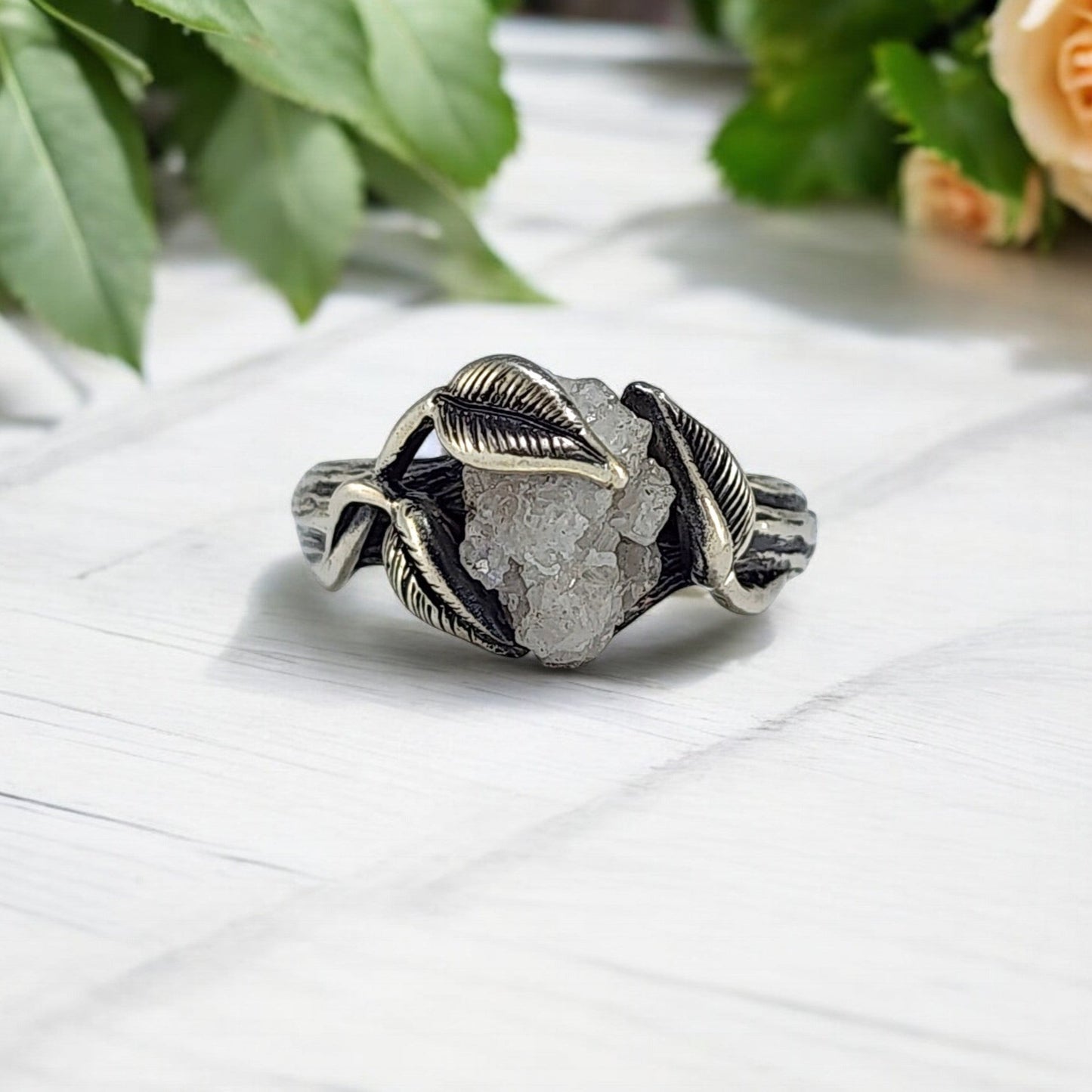 Silver ring with leaves on it, showing a raw rough diamond in the center