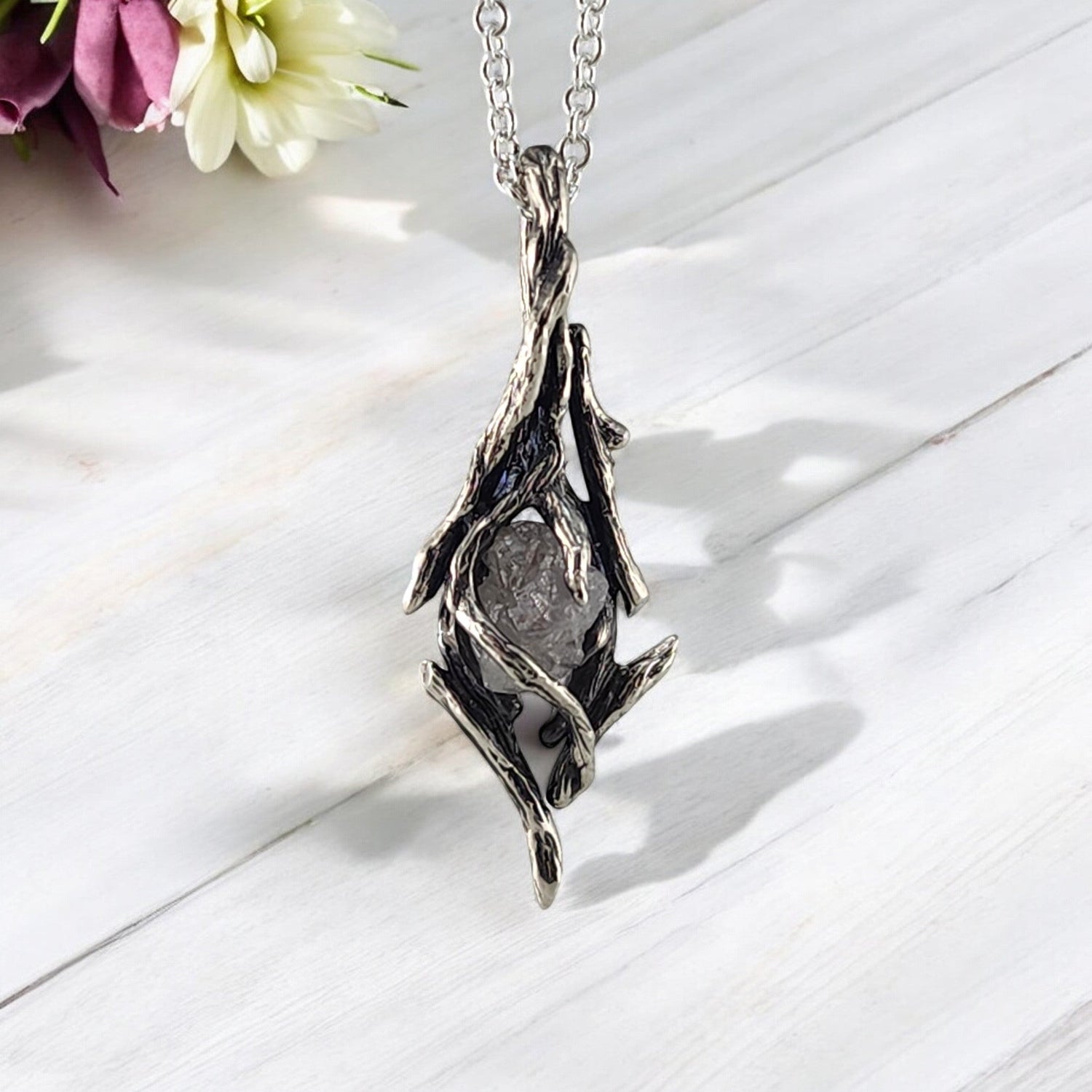 dark sterling silver pendant hanging down with a twig like design all around a raw diamond