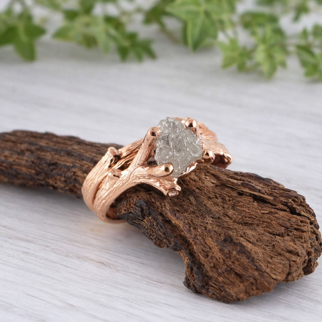 Rose gold ring with a raw diamond stone on a wooden surface with greenery in the background