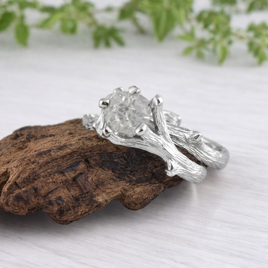 Silver ring with a large diamond on a wooden surface with greenery in the background