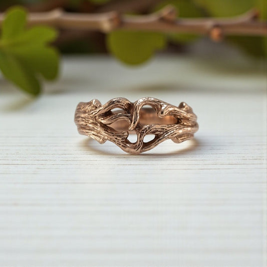 Rose gold branch-shaped ring on a light surface with green leaves in the background