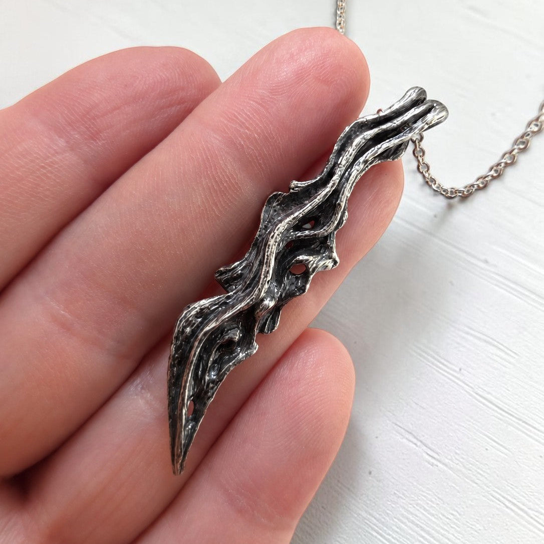 driftwood branch sterling silver pendant with oxidized finish to show wooden texture on a hand to show size