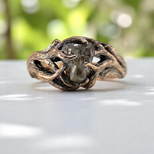 Rose gold ring with a central stone on a white surface with a blurred green background