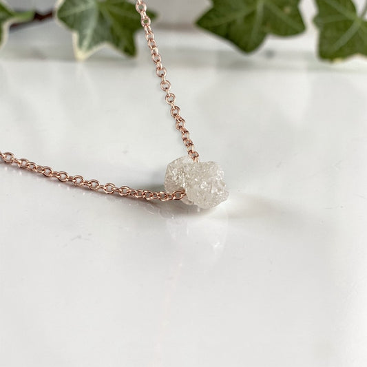 rose gold Necklace with a single raw diamond on a marble surface with ivy leaves in the background