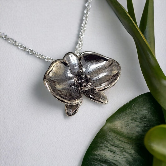 Silver orchid pendant necklace on a white background with green leaves.