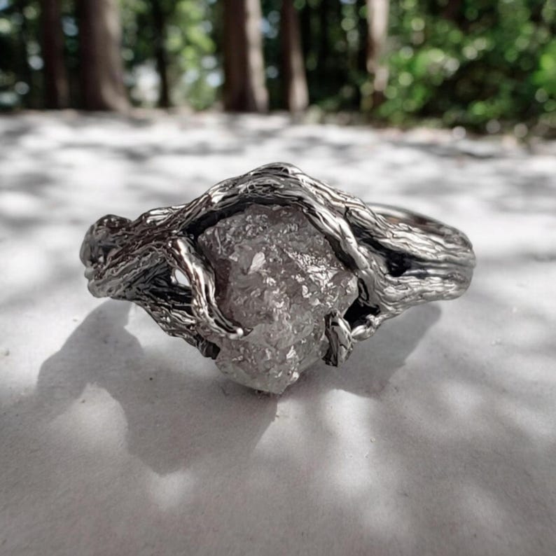 Antiqued White Gold Ring with a rough diamond on a textured surface with a natural background