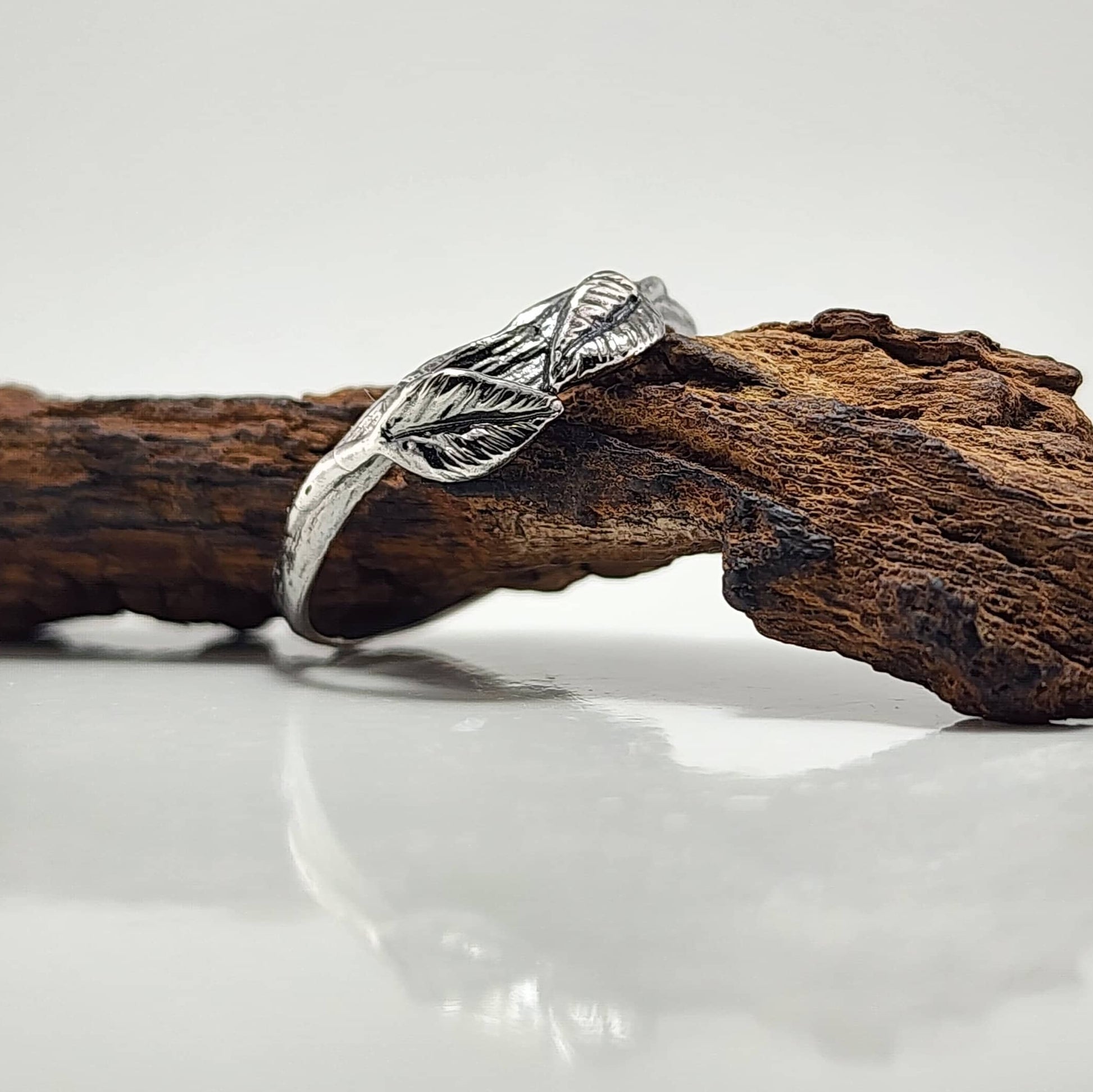 Silver leaf-patterned ring on a wooden branch with a white background