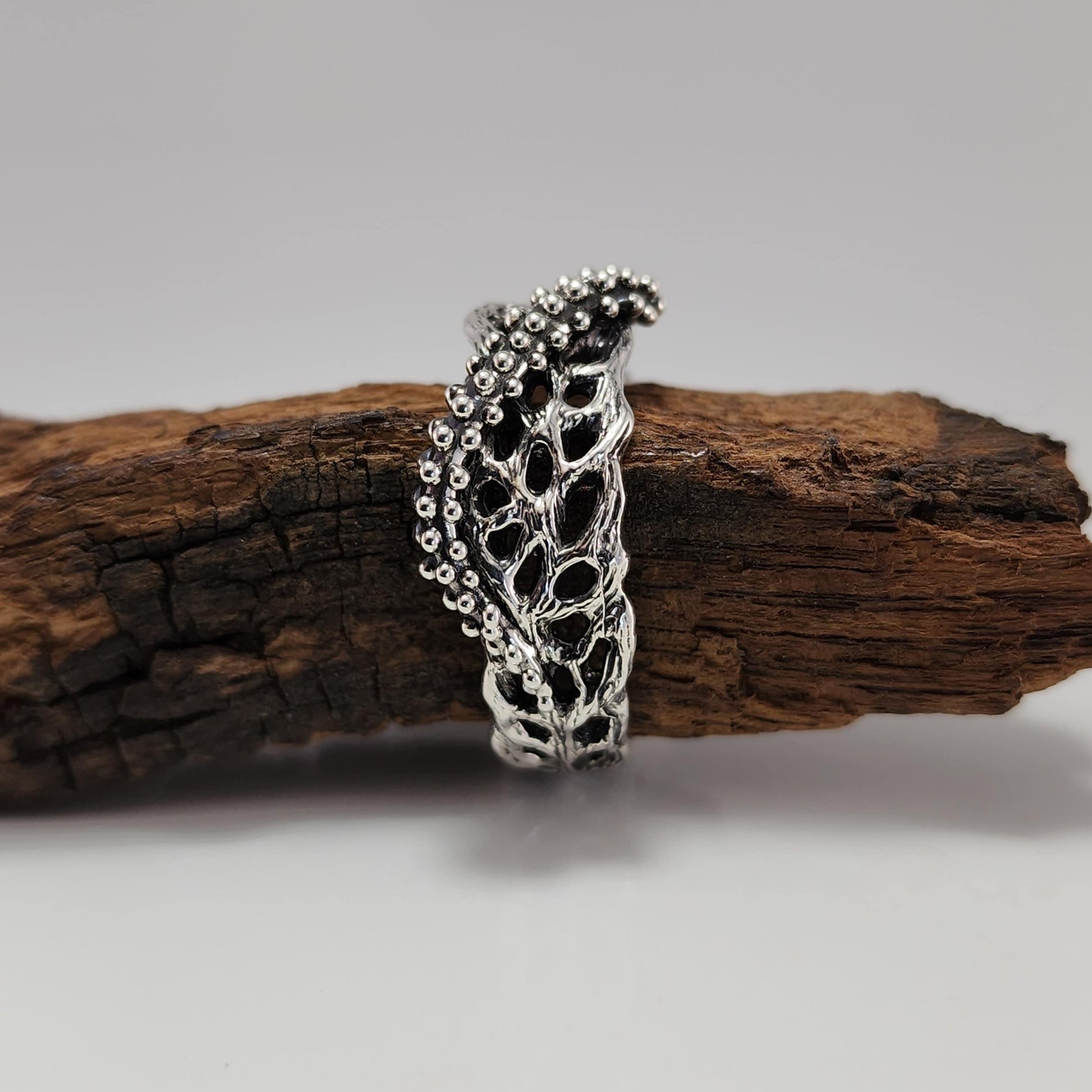 Silver ring with intricate starfish and seafan coral design on a wooden surface