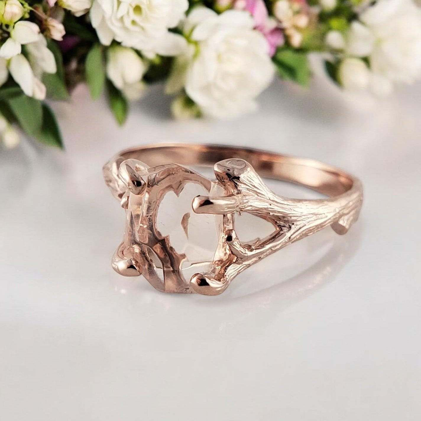 Rose gold ring with intricate design on a light background with flowers.