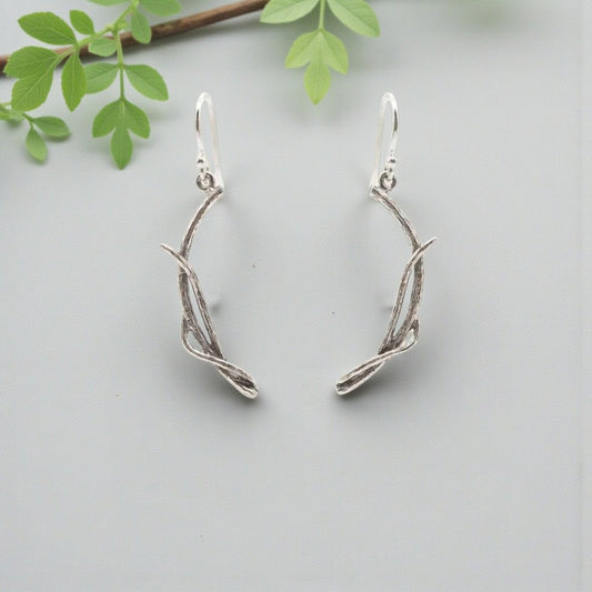 Silver branch-shaped earrings on a light gray background with green leaves.