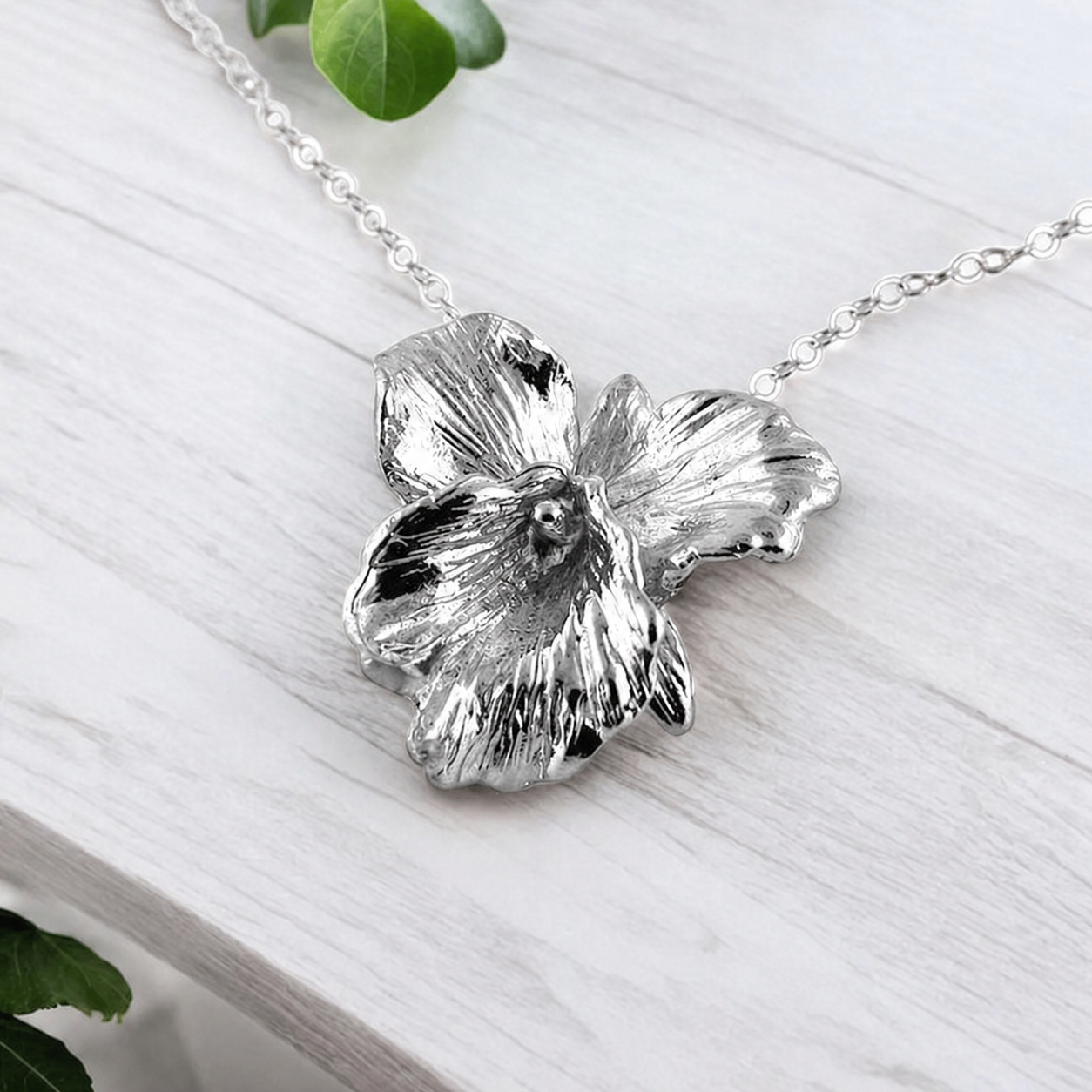 Silver flower-shaped pendant on a chain against a light wooden background