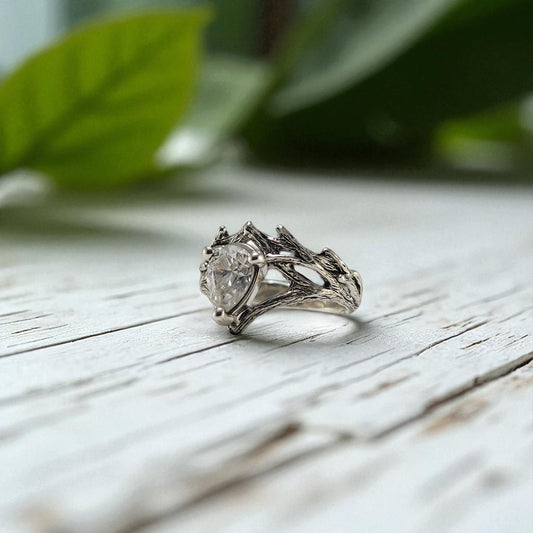 Silver ring with a diamond on a wooden surface with green leaves in the background