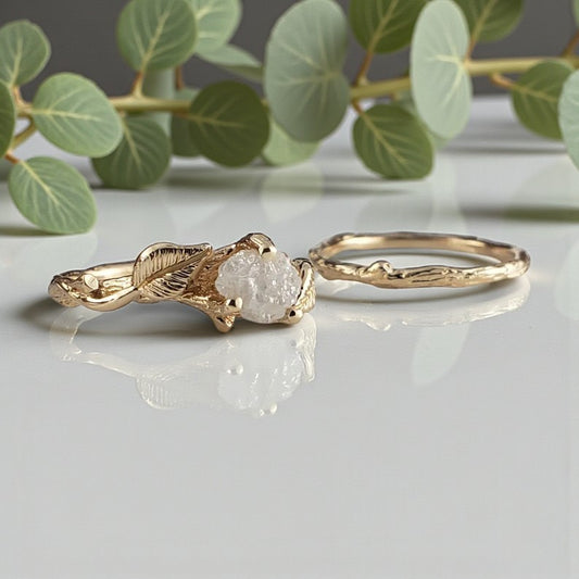 Gold ring with a centralraw diamond on a reflective surface with green leaves in the background
