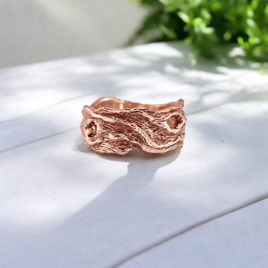 handmade driftwood style wedding ring in rose gold, lying on a wooden table